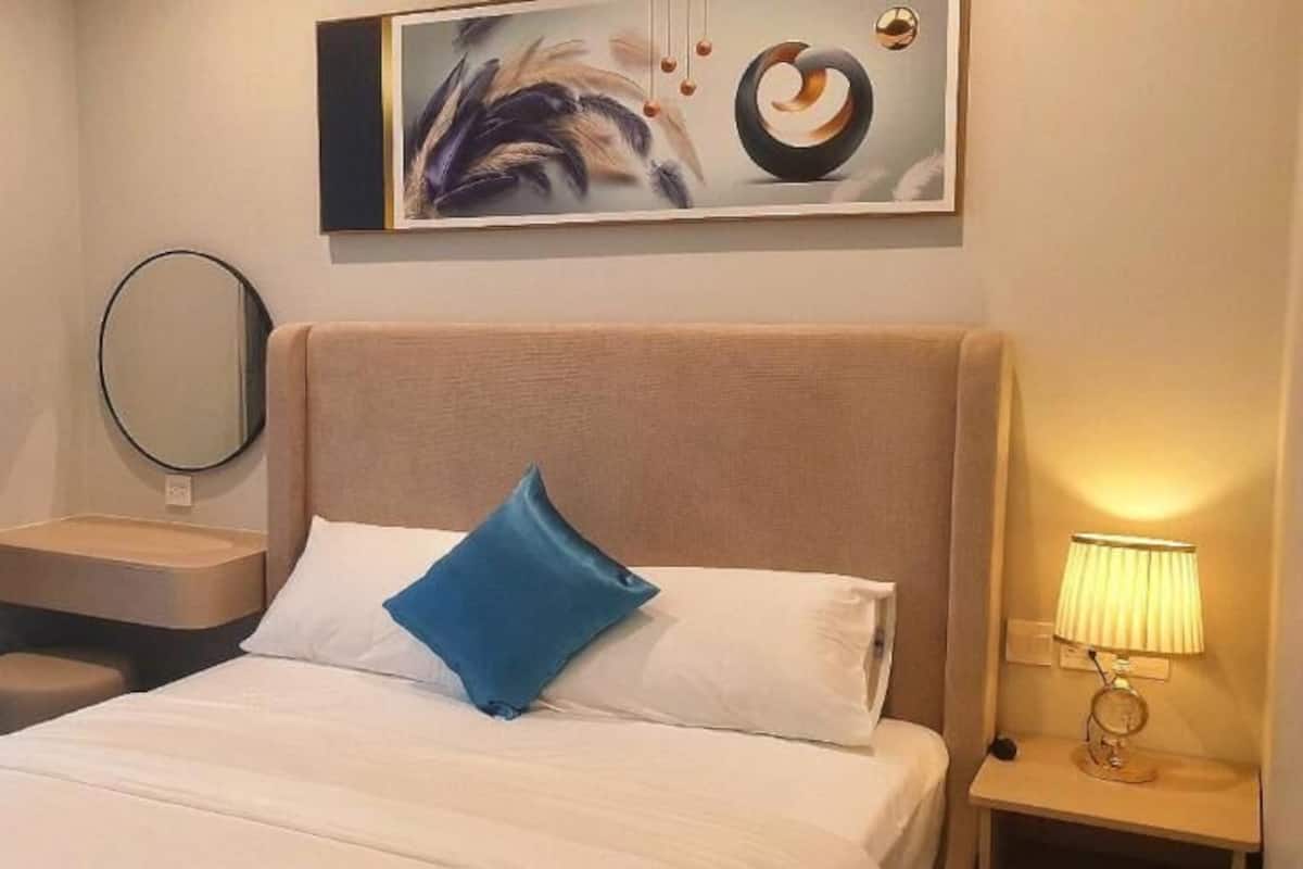 A hotel room with a bed, a bedside table with a lamp, a mirror, and a painting on the wall.