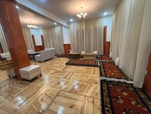 Um quarto amplo com piso de madeira polido, um sofá, um pequeno banquinho e um tapete estampado.