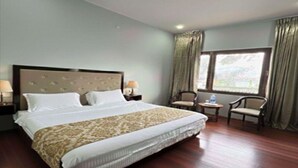 A hotel room with a large bed, two bedside tables with lamps, a window with curtains, and a chair by the window. - The Zurfi's Hotel (Kargil)