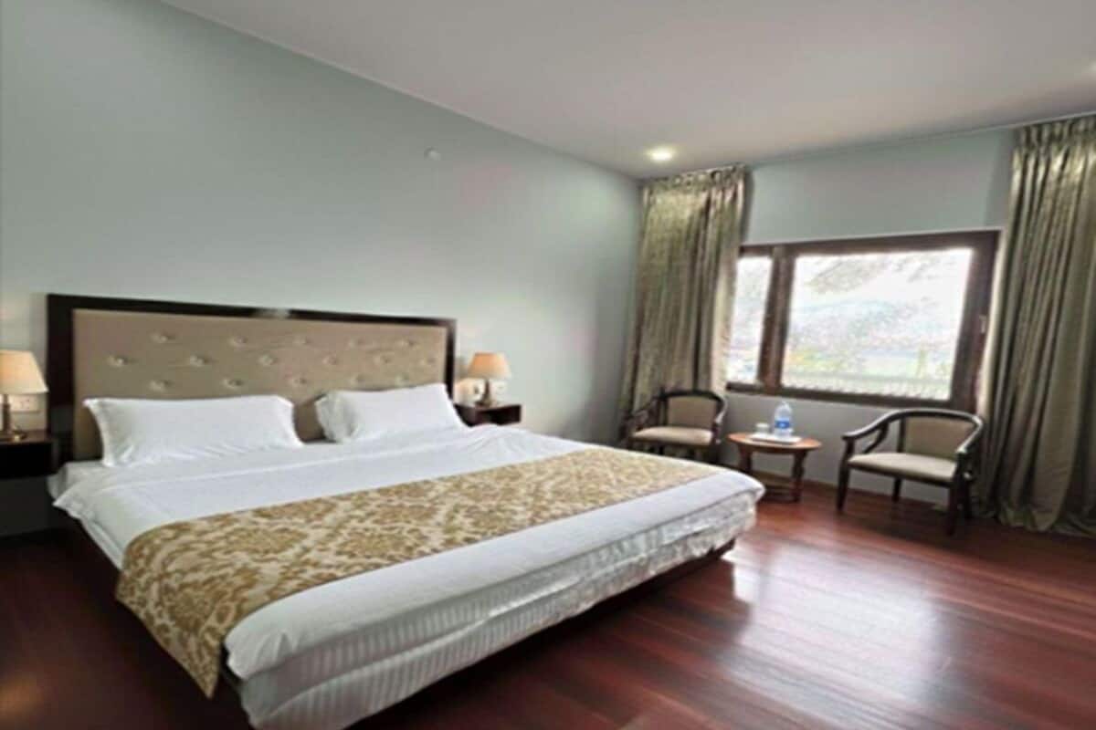 A hotel room with a large bed, two bedside tables with lamps, a window with curtains, and a chair by the window.