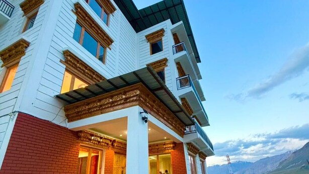 A multi-story building with a prominent entrance, a staircase leading to the main door, and a vehicle parked in front. - The Zurfi's Hotel (Kargil)