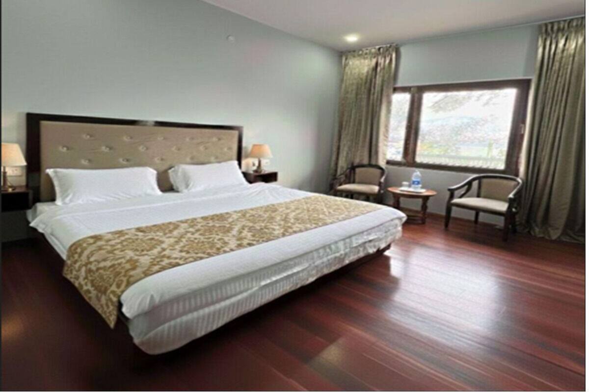 A hotel room with a large bed, a small table, two chairs, and a window with curtains.