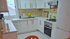 A kitchen with white cabinets, a gas stove, and a sink. There is a table with a patterned tablecloth and a decorative vase. - 2-Bedroom Apartment Puerto de la Cruz – Minimum Stay 4 Months, Quiet Location (Puerto de la Cruz)