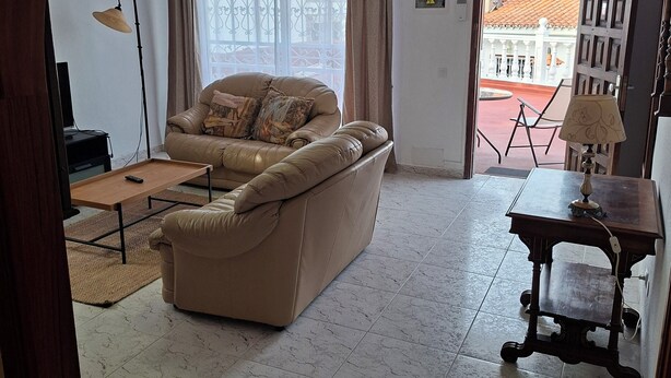 A living room with a sofa, a lamp, a table, and a view of a building outside. - 2-Bedroom Apartment Puerto de la Cruz – Minimum Stay 4 Months, Quiet Location (Puerto de la Cruz)