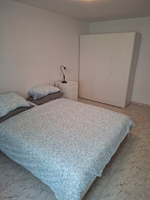 Ein Schlafzimmer mit einem großen Bett, einem Kleiderschrank und einem Nachttisch mit einer Lampe.