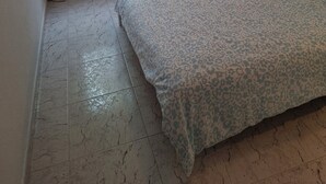 A bedroom with a bed, a nightstand with a lamp, a mirror, and a window with curtains. - 2-Bedroom Apartment Puerto de la Cruz – Minimum Stay 4 Months, Quiet Location (Puerto de la Cruz)