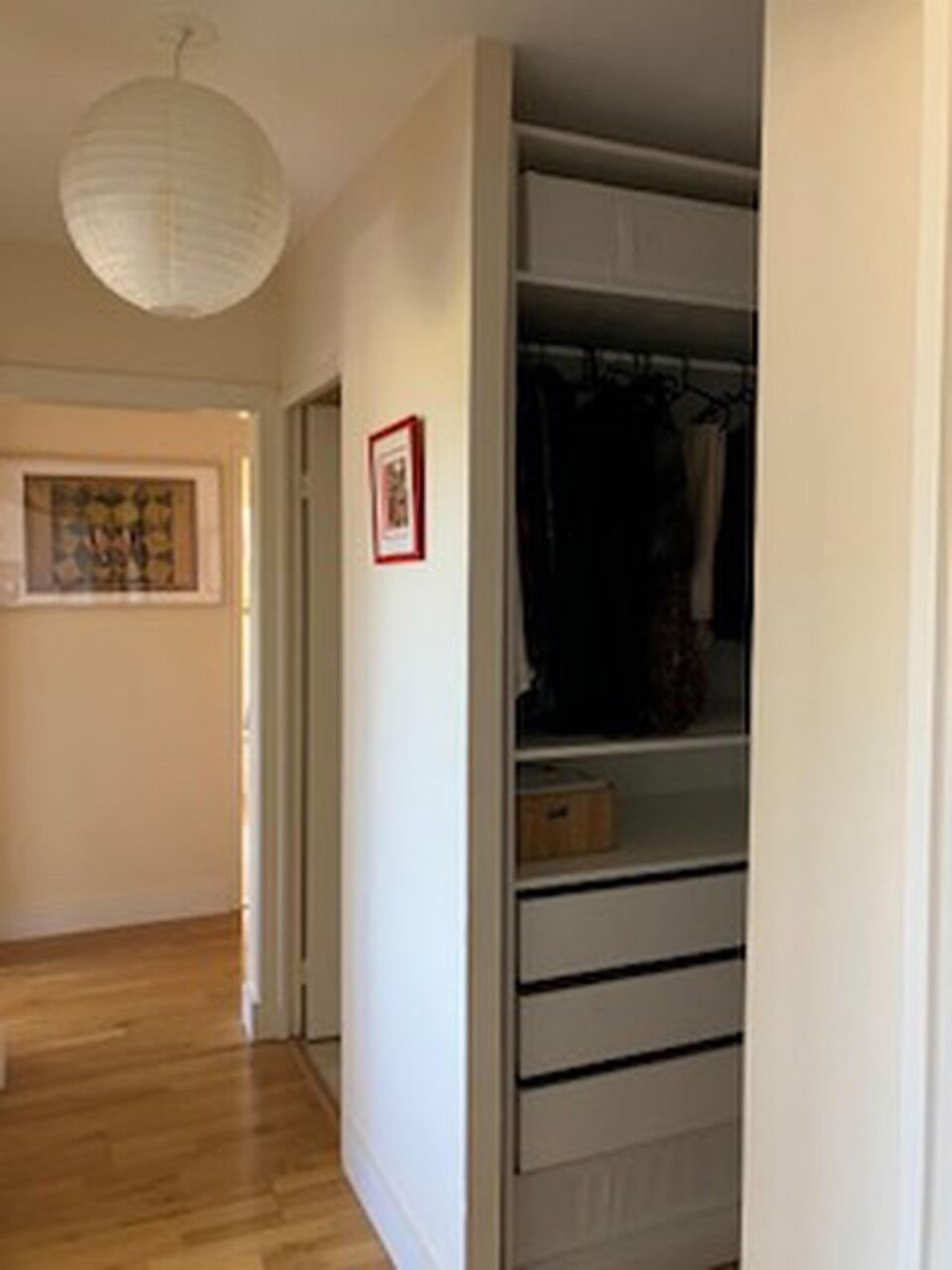 A hallway with a wooden floor, a white door, and a closet with hanging clothes and drawers.
