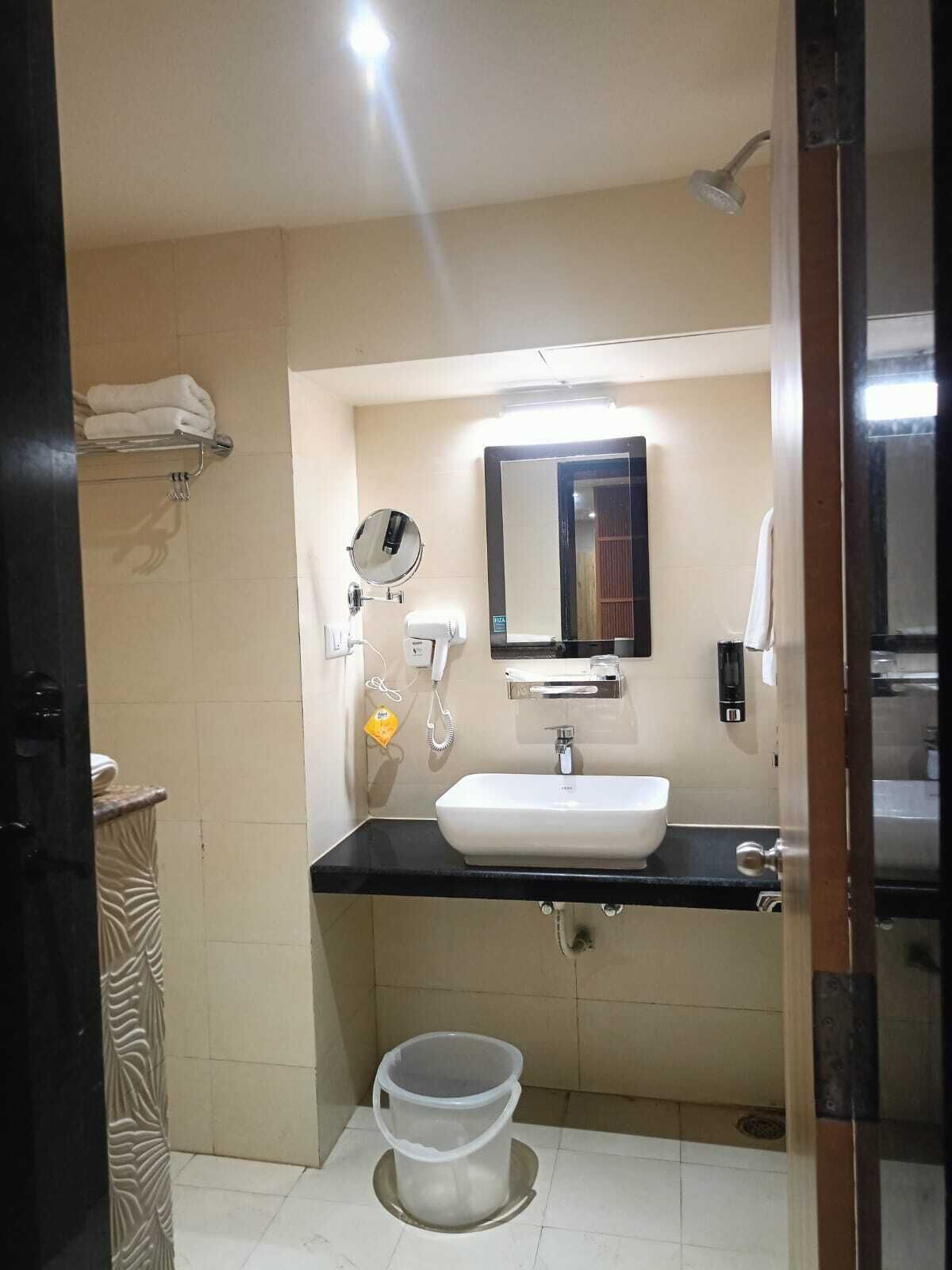 A bathroom with a white sink, a mirror, a towel rack, a shower, and a trash bin.