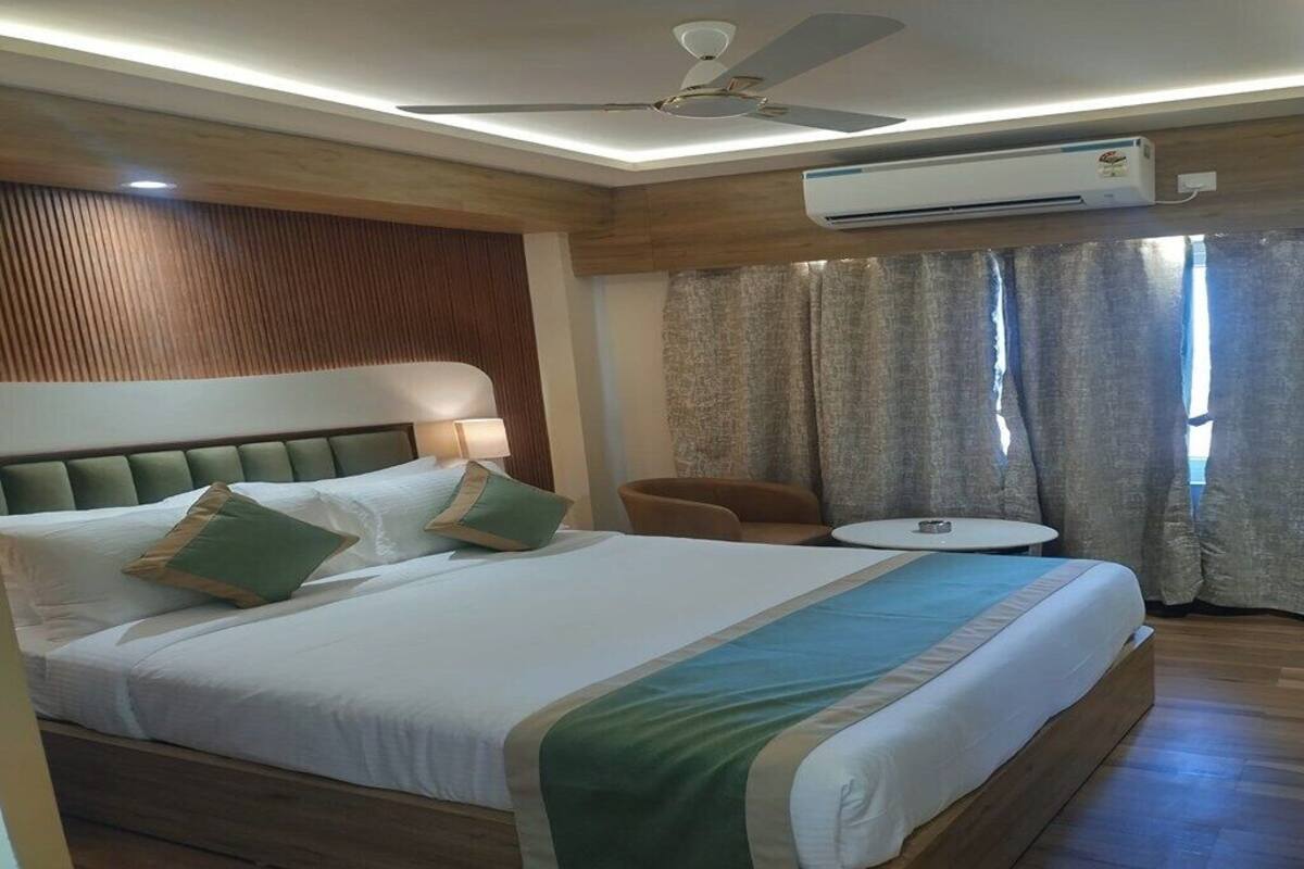 A hotel room with a large bed, a ceiling fan, an air conditioning unit, a small round table, and a chair.