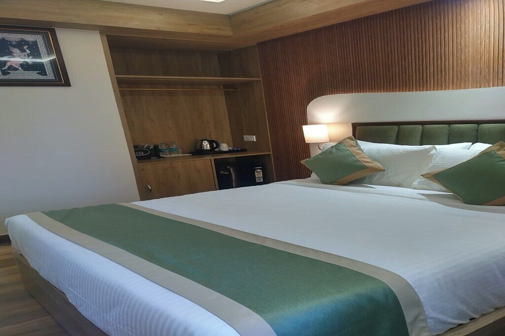 A hotel room with a large bed, wooden wardrobe, and a nightstand with a lamp.