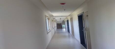 A long, narrow hallway with white walls and a light-colored floor, leading to a staircase at the end.