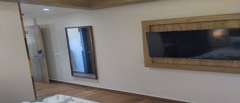 Une chambre d’hôtel avec un plancher en bois, un lit recouvert de draps blancs, un téléviseur à écran plat fixé au mur et un miroir au-dessus du téléviseur.