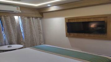 Habitación de hotel con cama, televisión montada en la pared, aire acondicionado, una mesita redonda y cortinas.