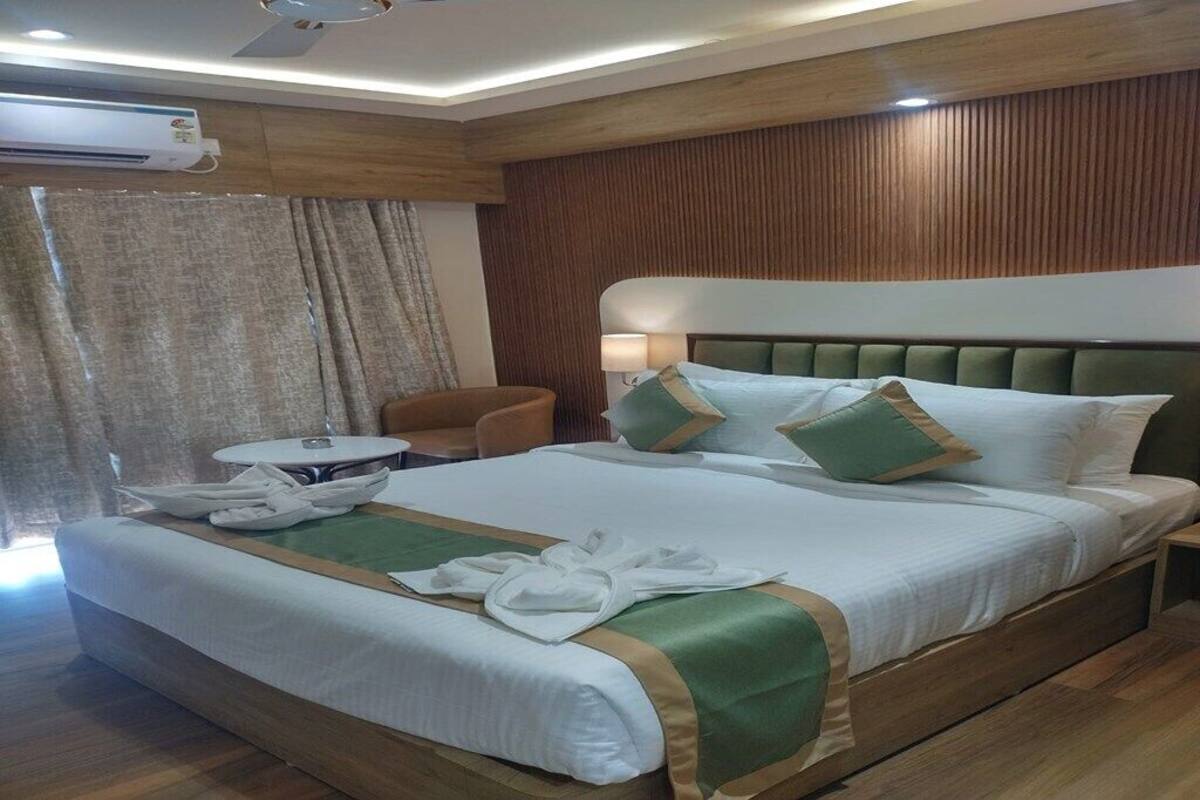 A hotel room with a large bed, a round table, a chair, and an air conditioning unit.
