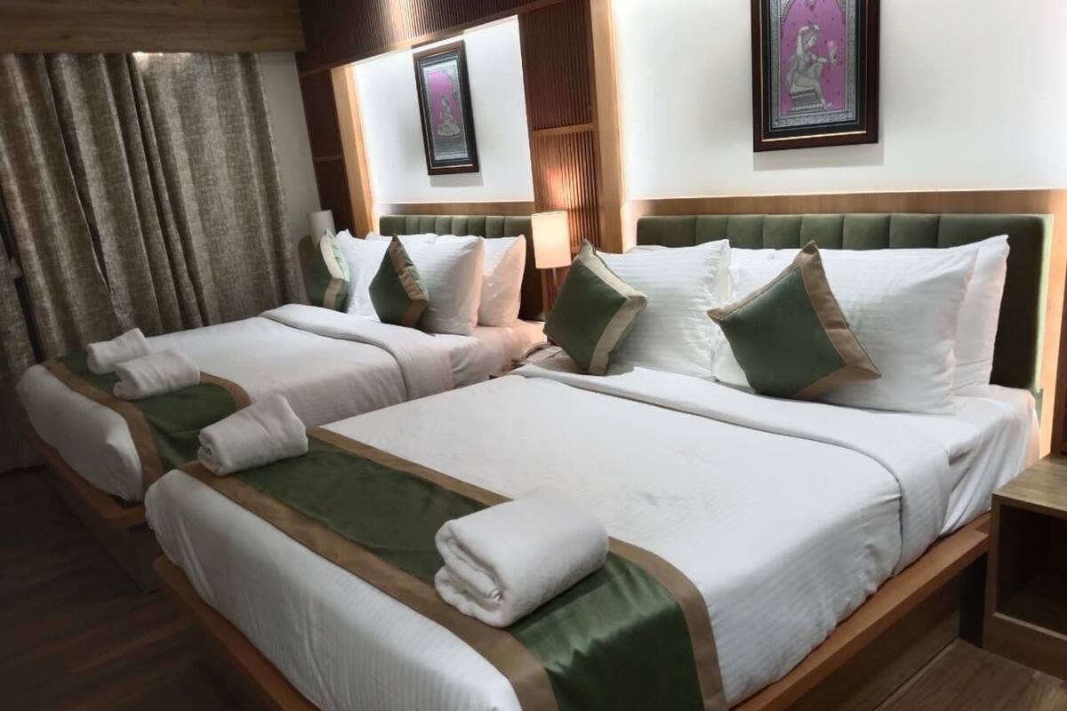 A hotel room with two beds, each with white linens and green accents, wooden headboards, and a wooden floor.