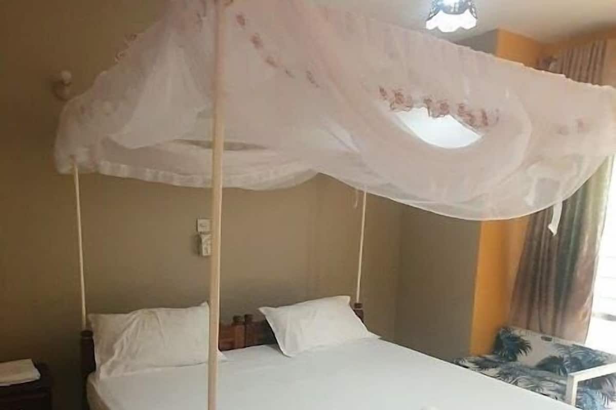 Una habitación con cama con dosel, ventilador de techo, mesita de noche y alfombra estampada.