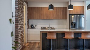 Une cuisine moderne avec des meubles en bois, un réfrigérateur en acier inoxydable et trois tabourets de bar.