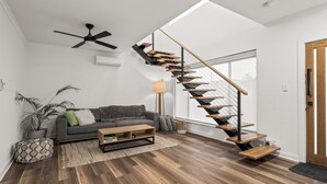 Un salon moderne avec un escalier en bois, un ventilateur de plafond et un canapé gris.