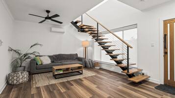 A modern living room with a wooden staircase, a ceiling fan, and a grey sofa.