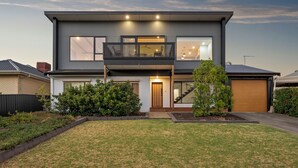 Une maison moderne à deux étages, dotée d’un balcon, de grandes fenêtres et d’une pelouse bien entretenue.