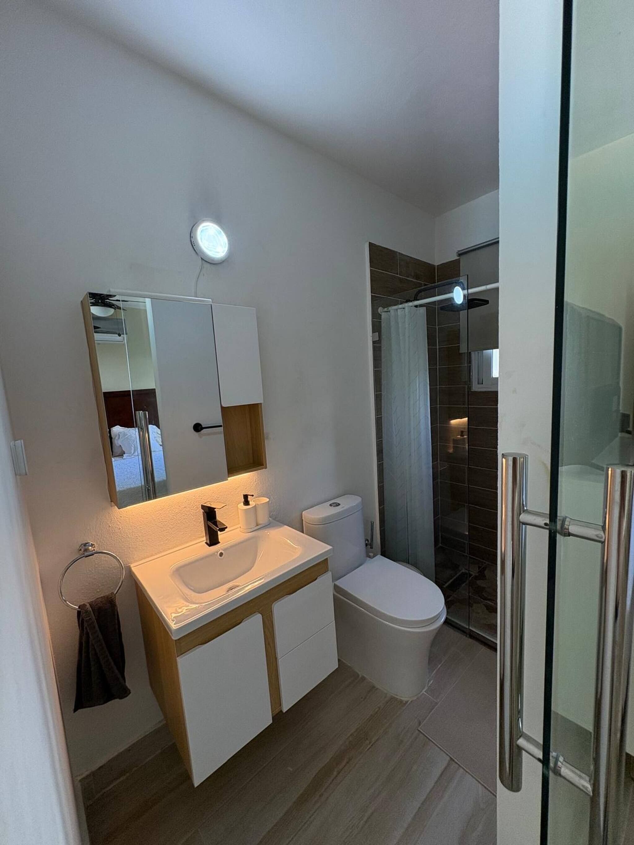 A modern bathroom with a white sink, mirror, and toilet. There is a glass shower enclosure with a glass door.