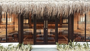 A building with a thatched roof, large glass windows, and a seating area with wicker furniture. - RAH GILI MALDIVES (Mahaanaelhihuraa)