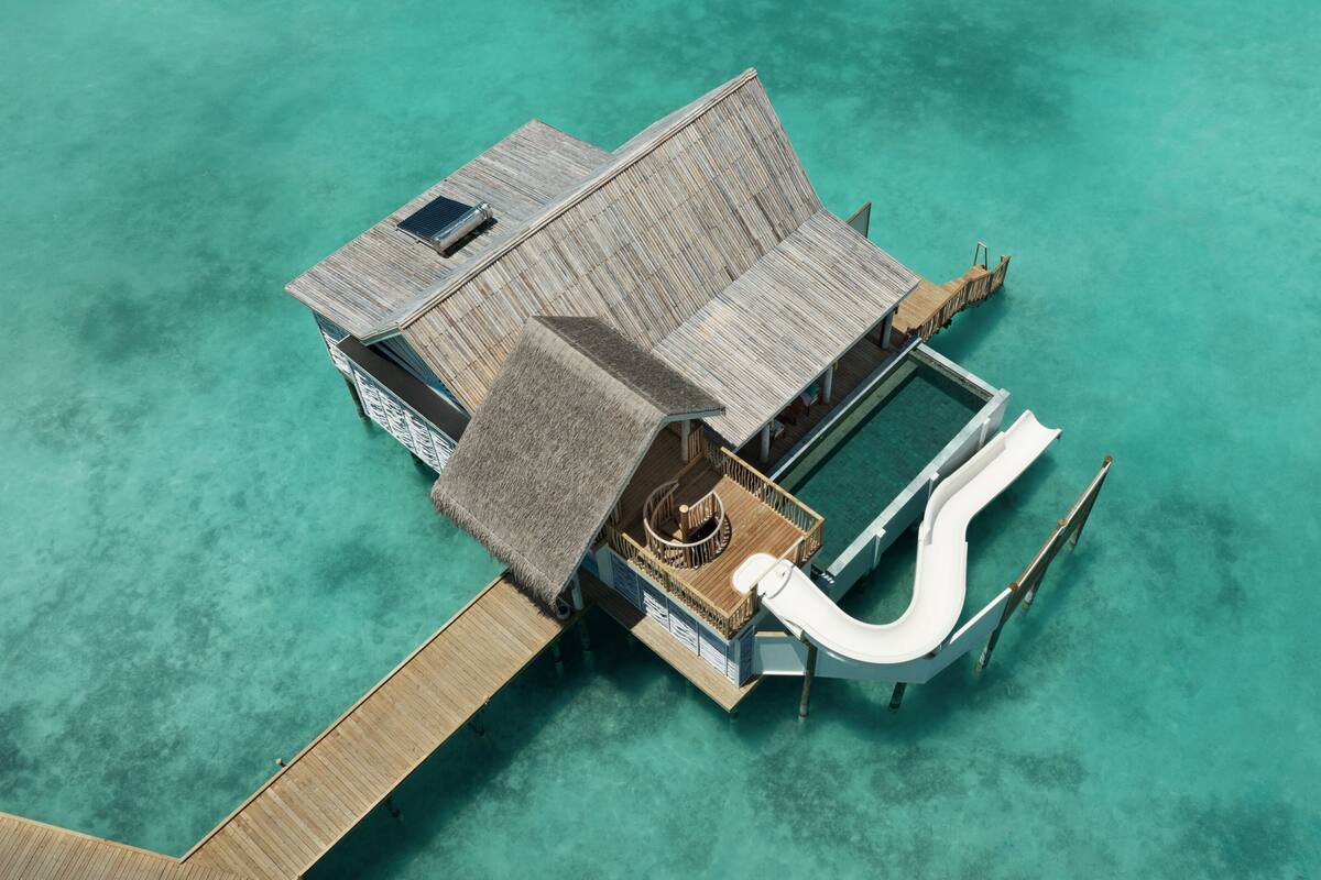 Una cabaña sobre el agua con techo de paja, piscina y tobogán.