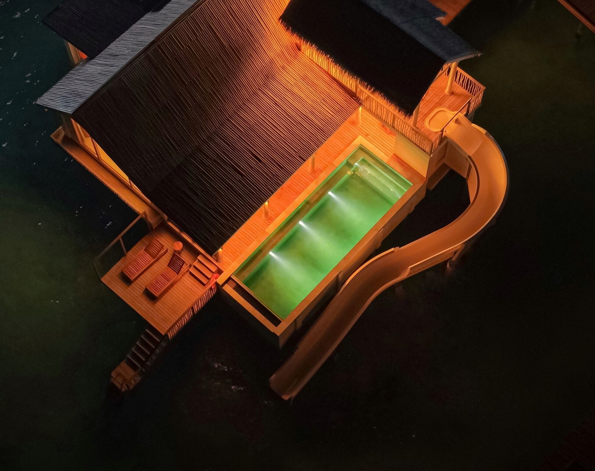 An overwater bungalow with a private pool, wooden deck, and lounge area.