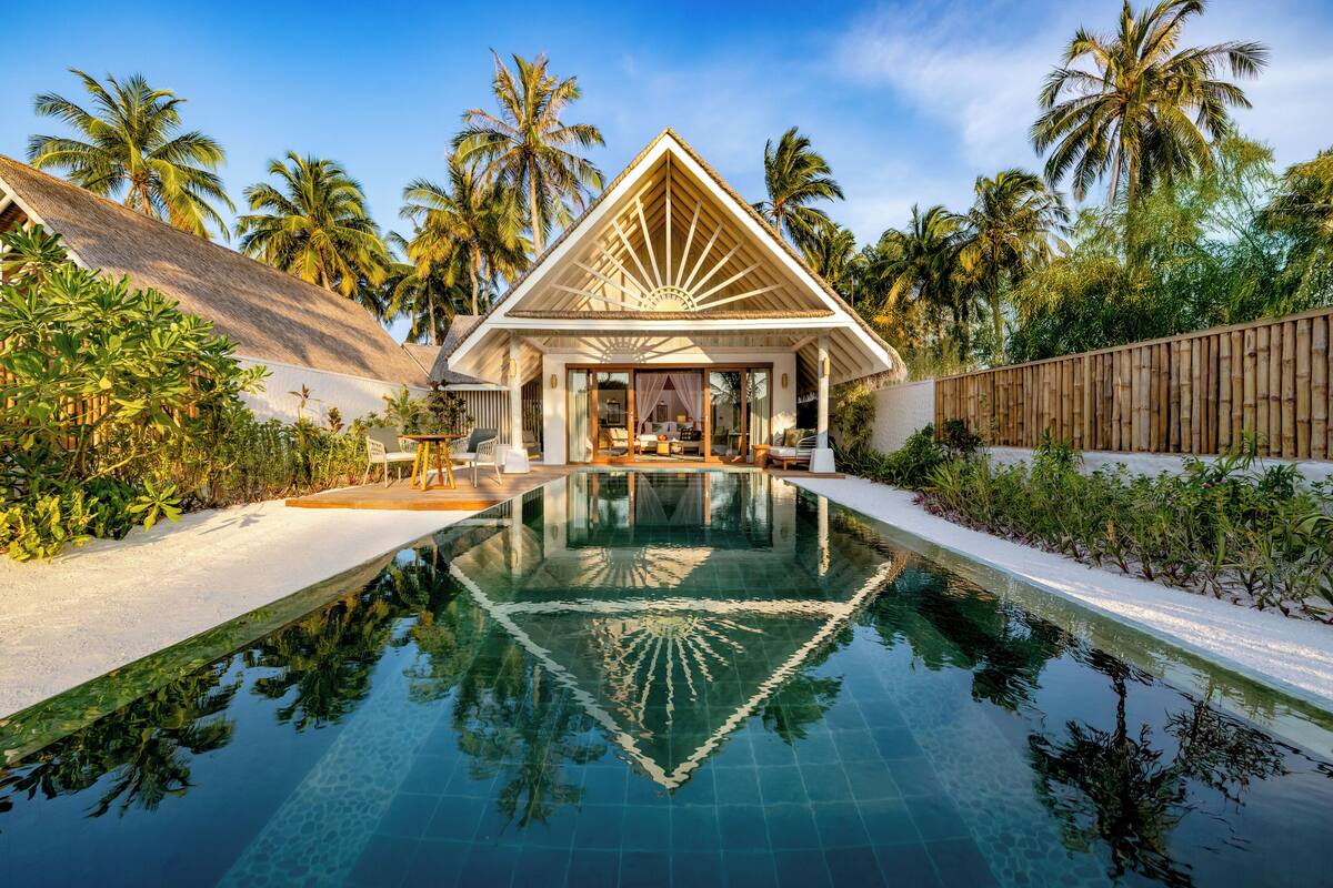 Un resort con piscina, palmeras y un edificio de techo de paja.