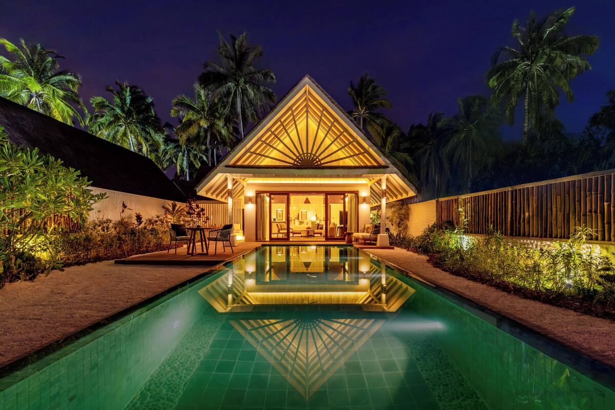 Un resort con piscina, palmeras y un edificio bien iluminado.