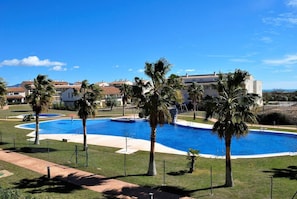 A large swimming pool surrounded by palm trees and a building complex in the background.