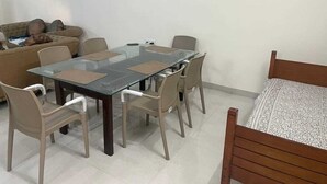 Une pièce comprenant une table à manger avec un plateau en verre, des chaises de couleur beige, un lit en bois et un canapé.
