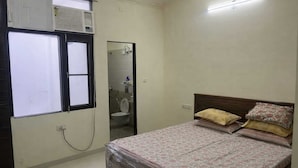 Une chambre à coucher comprenant un lit, une fenêtre, un climatiseur et une porte donnant accès à une salle de bain.