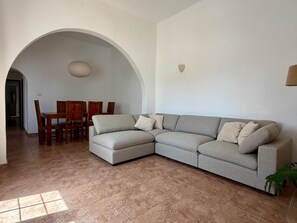A living room with a grey sectional sofa, a dining table with chairs, and a large arched doorway. - Villa Ann Lanzarote (Nazaret)
