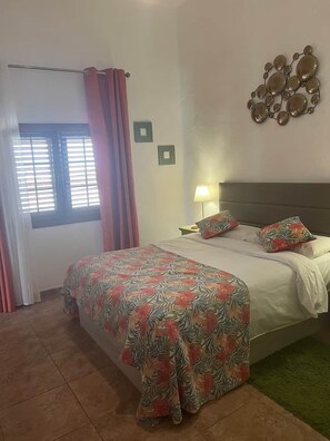 A bedroom with a bed, curtains, a wall-mounted lamp, and a decorative mirror. - Villa Ann Lanzarote (Nazaret)