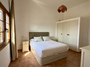 A bedroom with a bed, bedside table, lamp, wardrobe, and a hanging light fixture. - Villa Ann Lanzarote (Nazaret)