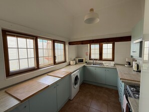 A compact kitchen with a washing machine, a microwave, and a stove. - Villa Ann Lanzarote (Nazaret)