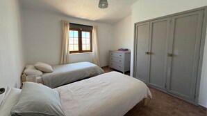 A bedroom with two beds, a dresser, a wardrobe, and a window with curtains. - Villa Ann Lanzarote (Nazaret)