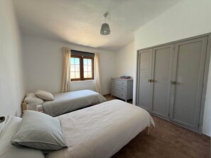 A bedroom with two beds, a dresser, a wardrobe, and a window with curtains. - Villa Ann Lanzarote (Nazaret)