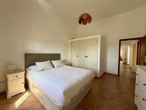 A bedroom with a bed, nightstand, wardrobe, and a hanging light fixture. - Villa Ann Lanzarote (Nazaret)