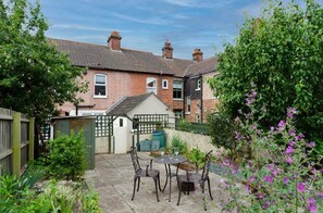 A residential backyard with a patio, chairs, a small shed, and a garden.