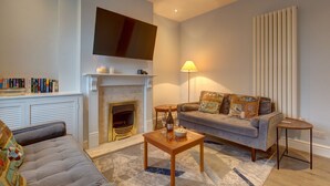 A living room with a fireplace, a sofa, a coffee table, and a television mounted on the wall. - Beecroft Cottage - sleeps 4 guests  in 2 bedrooms (Cromer)