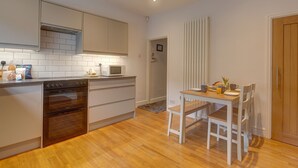 A modern kitchen with a built-in oven, microwave, and white cabinets. There is a dining table with chairs and a small breakfast setup. - Beecroft Cottage - sleeps 4 guests  in 2 bedrooms (Cromer)