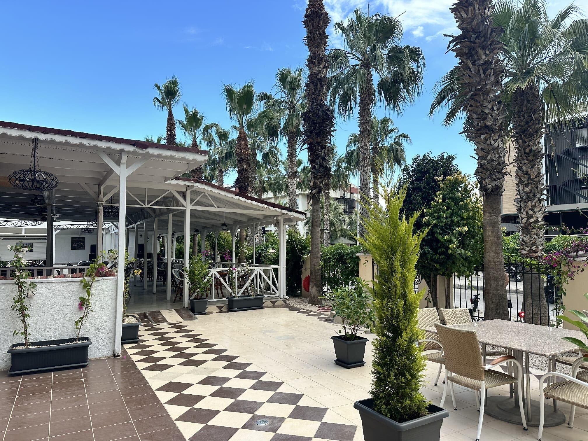 Une terrasse extérieure couverte, dotée d’un sol à carreaux, de palmiers et de mobilier d’extérieur.