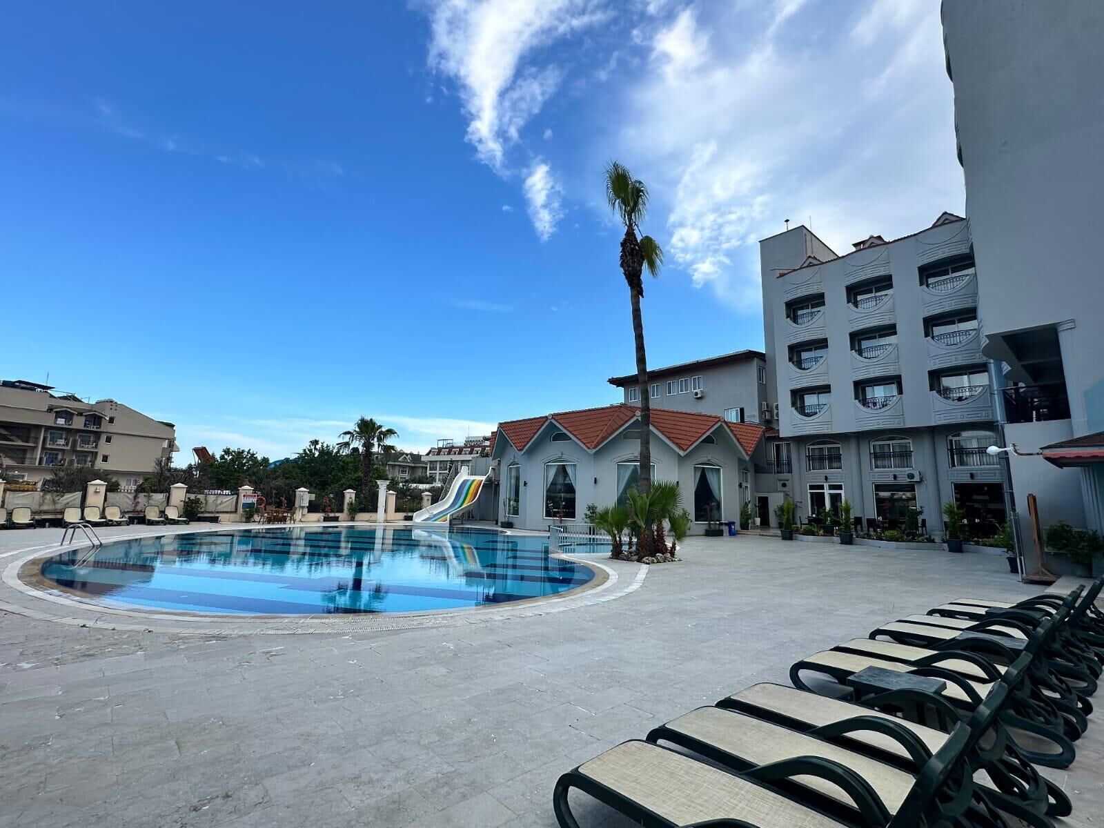Una piscina con sillas de descanso, una palmera y un edificio con balcones.