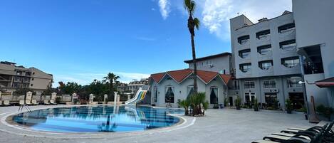 Una piscina con sillas de descanso, una palmera y un edificio con balcones.