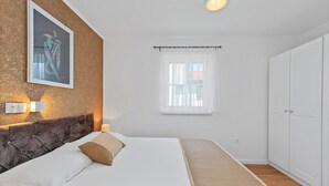 Un dormitorio con cama, cabecera, ventana con cortinas, armario y un cuadro en la pared.