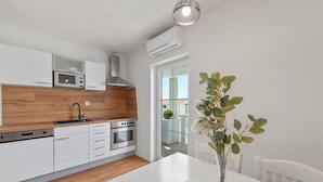 Una cocina moderna con armarios blancos, microondas integrado, campana de acero inoxidable y una zona de comedor con mesa y sillas blancas.