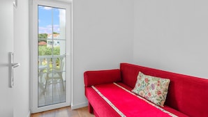 Un sofá rojo con un cojín floral en una habitación con una puerta blanca que da a un balcón.