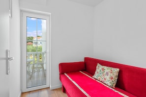 A red sofa with a floral pillow in a room with a white door leading to a balcony. - Superior Apartment Tania 8 (Sveti Filip i Jakov)